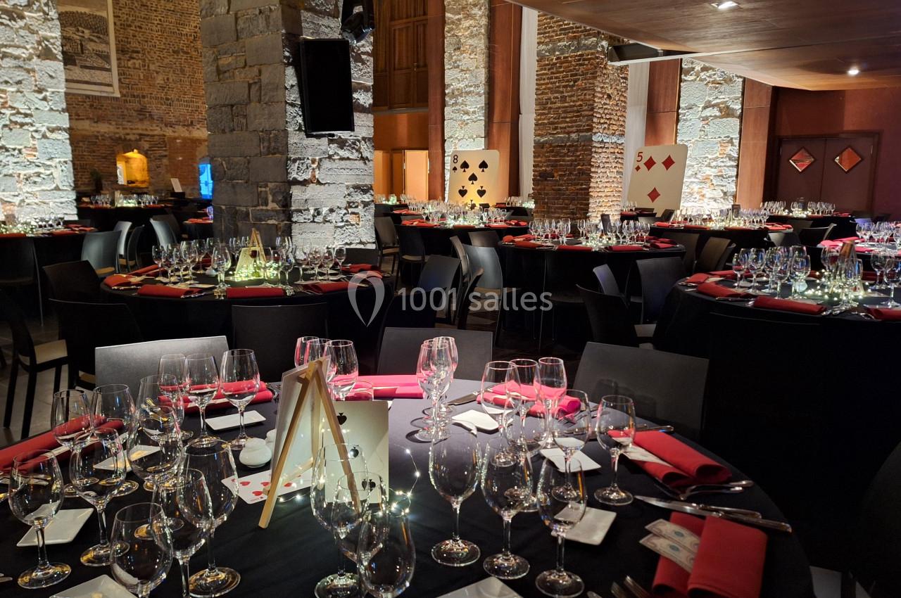 Location salle Anhée (Namur) - Ferme de l'Abbaye de Moulins #9 Salle de réception élégante avec tables rondes dressées, nappes noires, serviettes rouges et décorations sur le thème des…