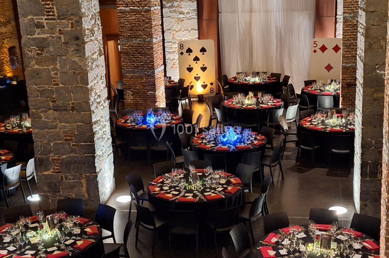 Location salle Anhée (Namur) - Ferme de l'Abbaye de Moulins #8 Salle de réception décorée sur le thème des cartes, avec des tables rondes dressées et éclairages colorés.