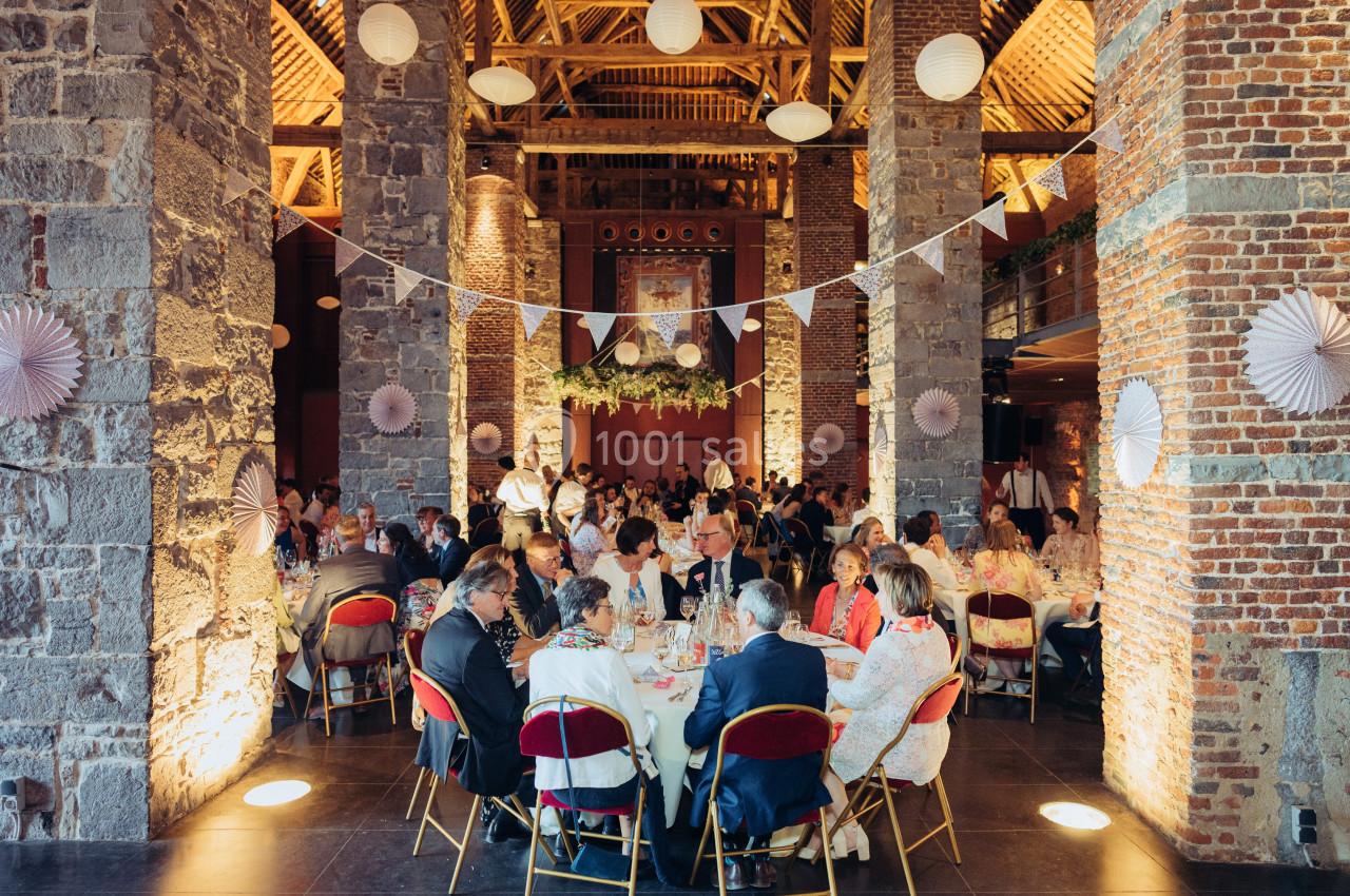 Location salle Anhée (Namur) - Ferme de l'Abbaye de Moulins #20 Salle en pierre et briques avec des invités assis à des tables rondes décorées pour un événement festif.