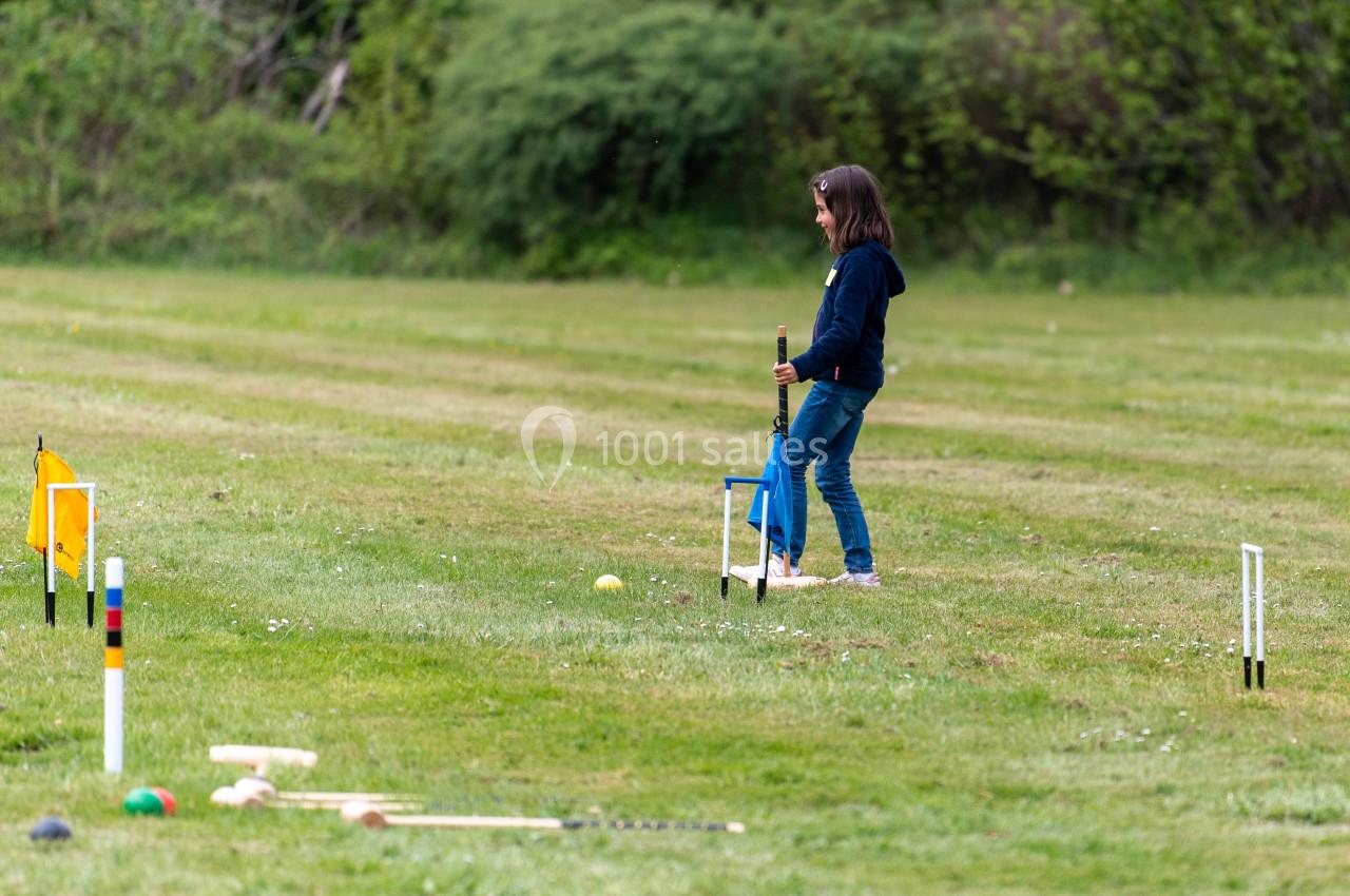 Location salle Anhée (Namur) - Ferme de l'Abbaye de Moulins #16 Une jeune fille joue au croquet sur une pelouse, entourée de piquets et de maillets.