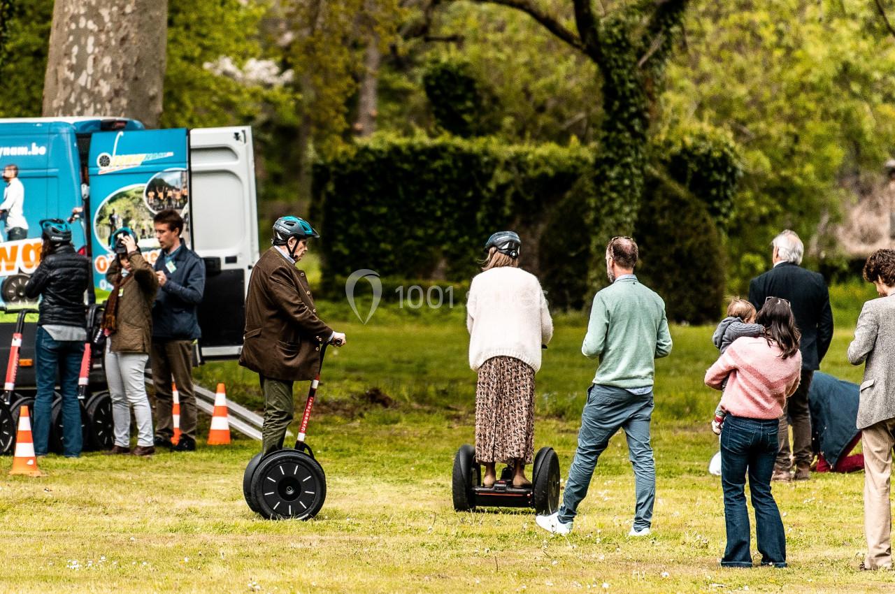 Location salle Anhée (Namur) - Ferme de l'Abbaye de Moulins #17 Des personnes testent des gyropodes sur une pelouse, avec un camion promotionnel et des cônes en arrière-plan.