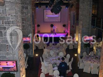 Location salle Anhée (Namur) - Ferme de l'Abbaye de Moulins #32 Salle de réception avec tables dressées et scène éclairée pour une présentation ou un spectacle.