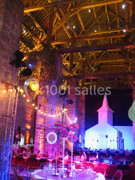 Location salle Anhée (Namur) - Ferme de l'Abbaye de Moulins #33 Intérieur d'une grange aménagée avec éclairages colorés, tables dressées et décorations festives, incluant une maquette d…