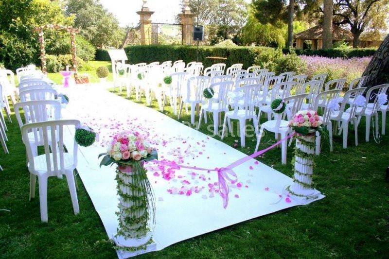 Allée décorée de pétales roses et de fleurs blanches, entourée de chaises blanches, pour une cérémonie en extérieur.