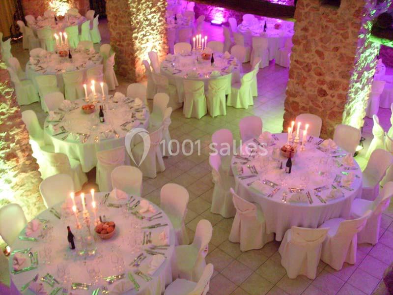 Salle de réception décorée avec des tables rondes élégantes, nappes blanches, chandeliers et éclairage coloré.