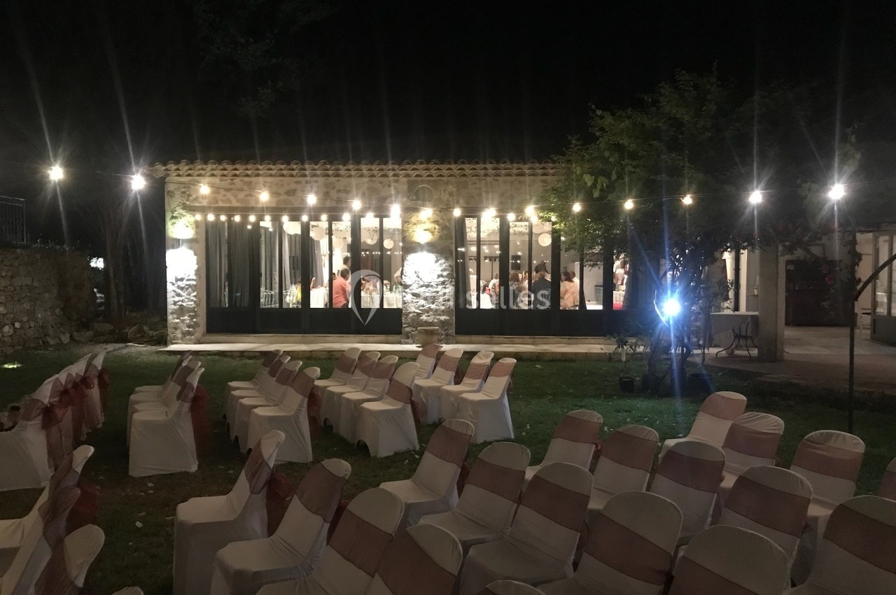 Salle éclairée en soirée avec des chaises disposées à l'extérieur, probablement pour un événement.