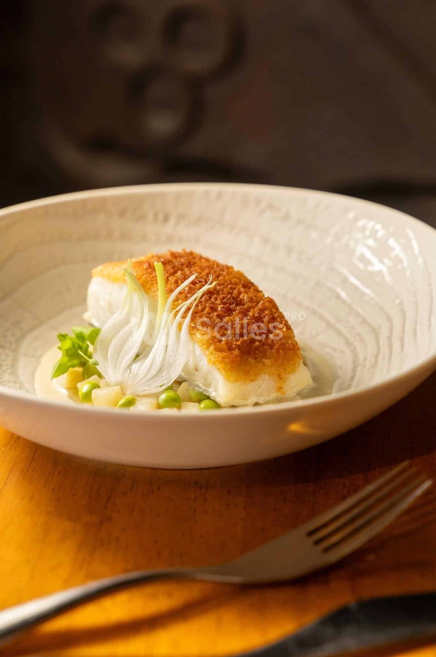 Filet de poisson pané servi sur une sauce crémeuse avec petits pois, oignons émincés et herbes fraîches dans une assiette…