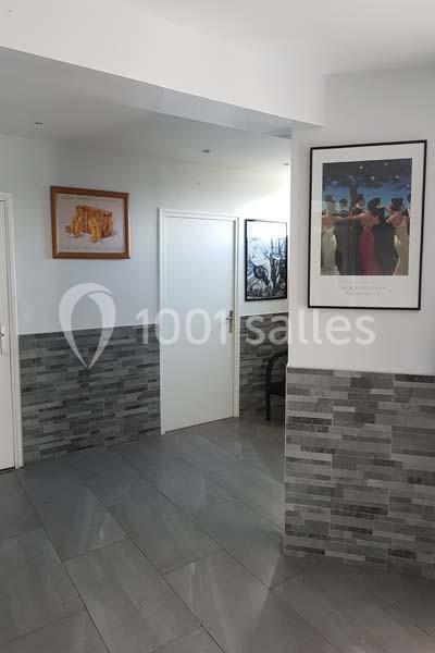 Location salle Nanteuil-lès-Meaux (Seine-et-Marne) - Centre D #26 Un couloir intérieur avec murs carrelés gris, portes blanches et cadres décoratifs accrochés aux murs.
