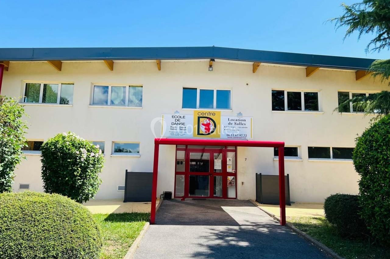 Location salle Nanteuil-lès-Meaux (Seine-et-Marne) - Centre D #28 Façade d'un bâtiment avec entrée principale rouge, entourée de verdure et sous un ciel dégagé.