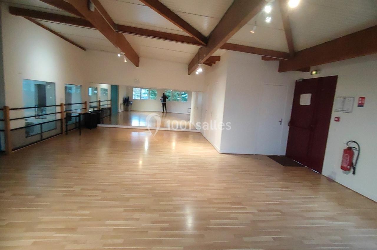 Location salle Nanteuil-lès-Meaux (Seine-et-Marne) - Centre D #21 Salle lumineuse avec parquet en bois, miroirs sur un mur, barres de danse et poutres apparentes au plafond.