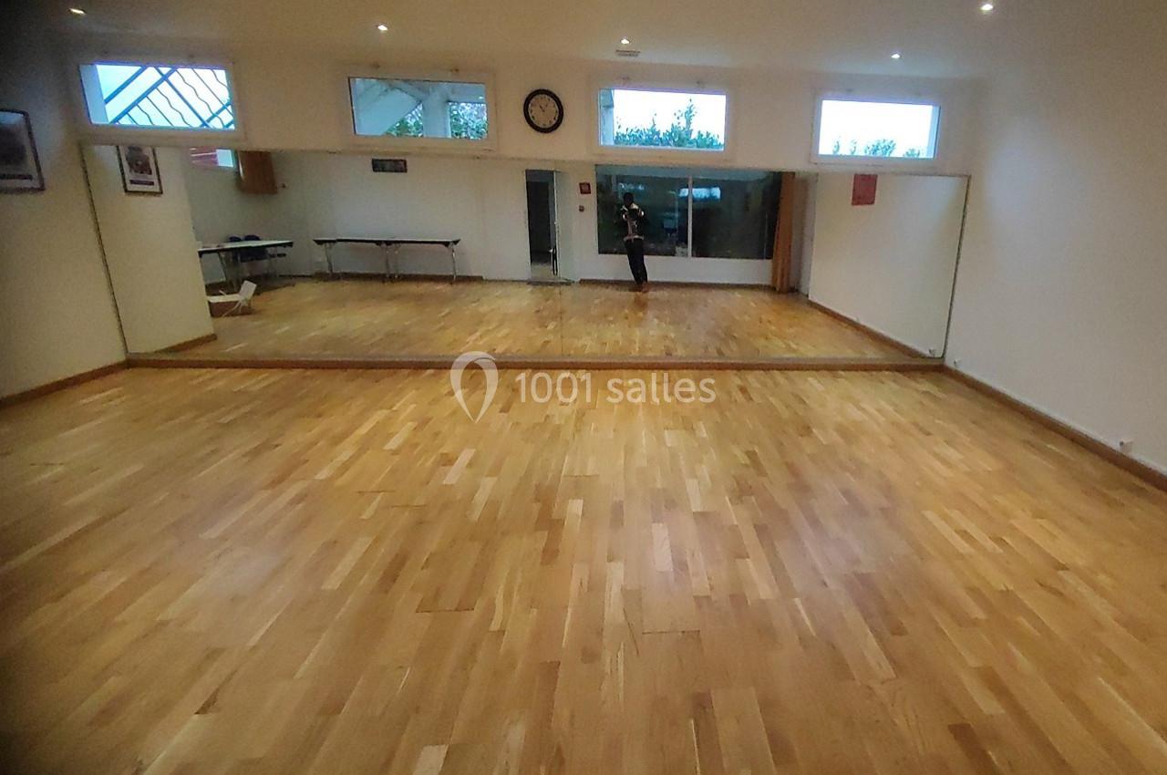 Location salle Nanteuil-lès-Meaux (Seine-et-Marne) - Centre D #23 Salle avec parquet en bois clair, grand miroir mural, fenêtres en hauteur et mobilier minimaliste en arrière-plan.