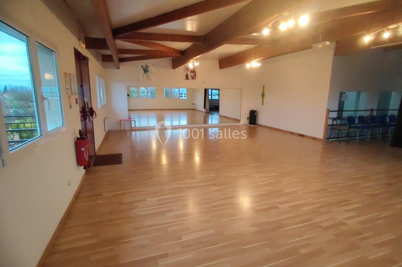 Location salle Nanteuil-lès-Meaux (Seine-et-Marne) - Centre D #20 Salle lumineuse avec parquet en bois, murs blancs, grandes fenêtres et plafond avec poutres apparentes.
