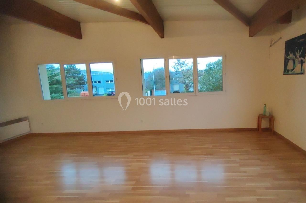 Location salle Nanteuil-lès-Meaux (Seine-et-Marne) - Centre D #24 Salle vide avec parquet en bois, murs clairs, grandes fenêtres laissant entrer la lumière naturelle et poutres apparentes.