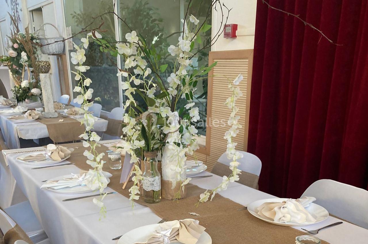 Location salle Nanteuil-lès-Meaux (Seine-et-Marne) - Centre D #14 Décoration de table avec nappes blanches, chemins de table en toile de jute et un vase d'orchidées blanches.