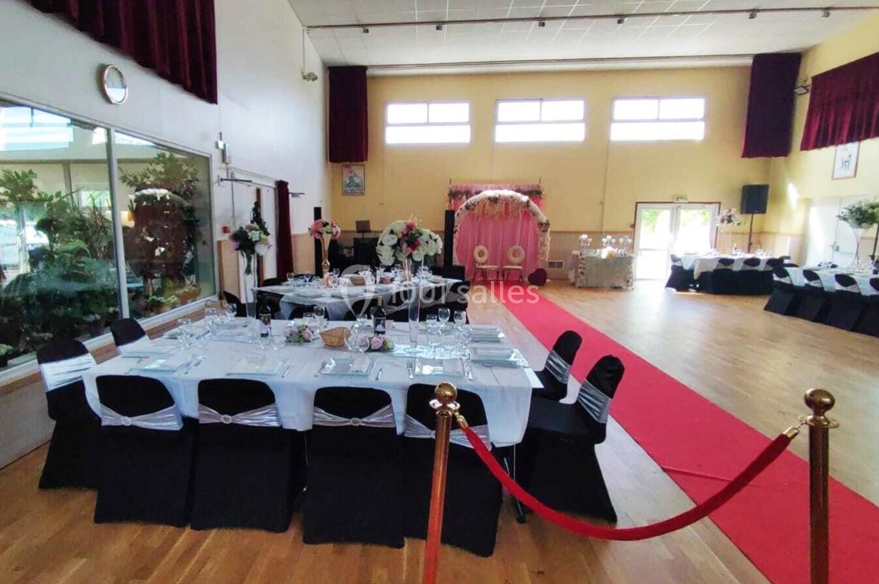 Location salle Nanteuil-lès-Meaux (Seine-et-Marne) - Centre D #2 Salle de réception décorée pour un événement, avec tables dressées, allée rouge et arche fleurie au fond.