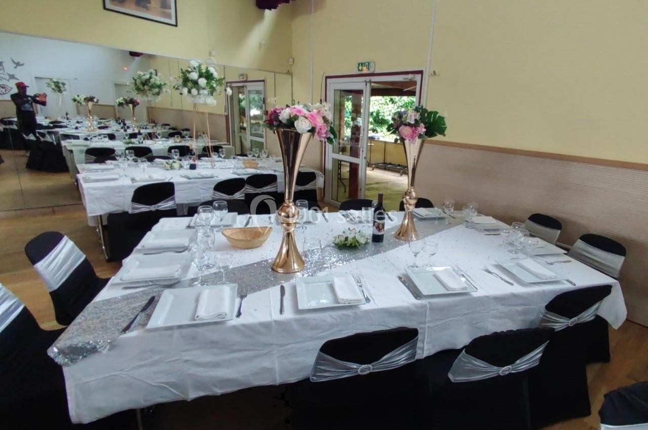 Location salle Nanteuil-lès-Meaux (Seine-et-Marne) - Centre D #7 Salle décorée pour un événement avec tables dressées, nappes blanches, centres de table fleuris et chaises noires ornées.