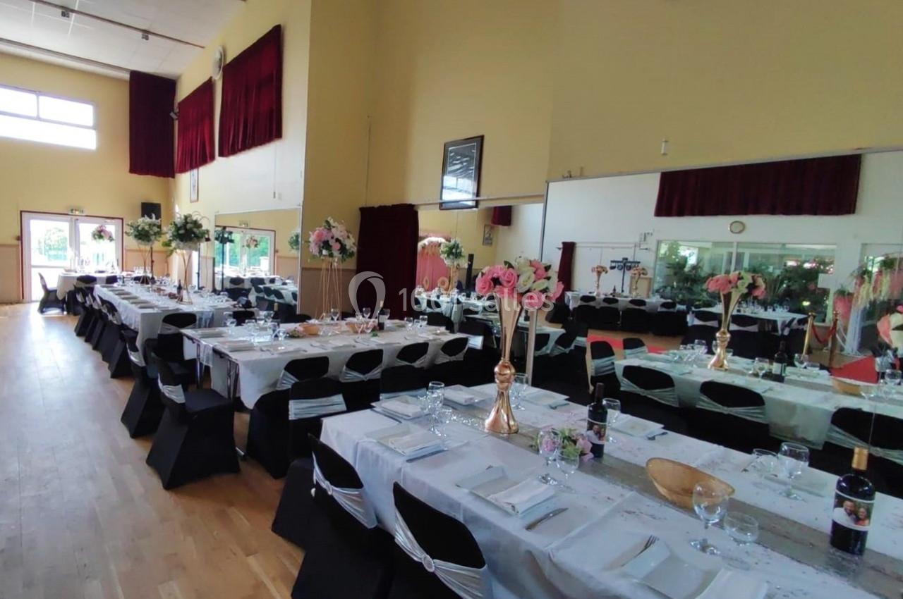 Location salle Nanteuil-lès-Meaux (Seine-et-Marne) - Centre D #11 Salle de réception décorée avec des tables alignées, nappes blanches, chaises noires et arrangements floraux roses.