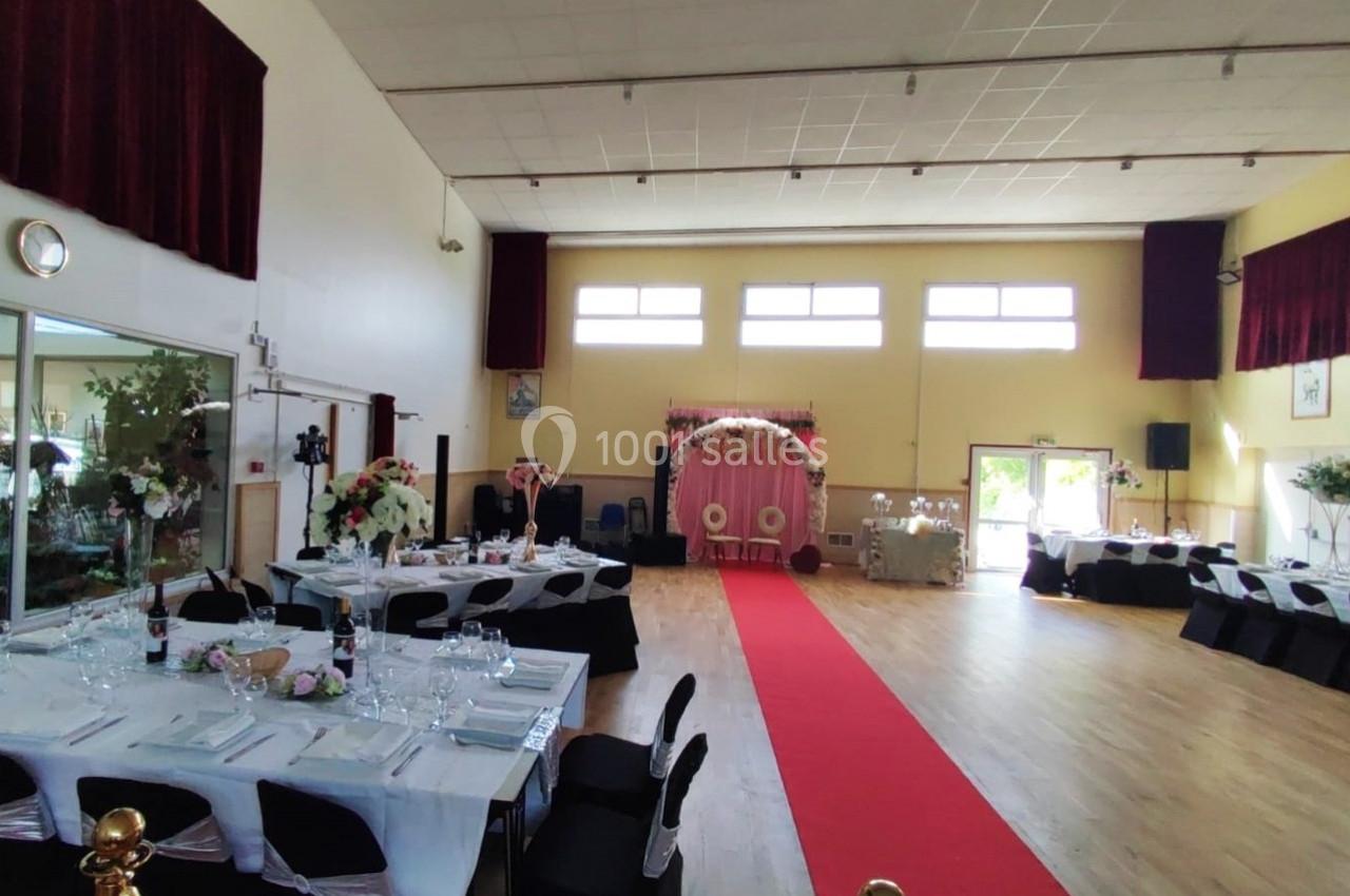 Location salle Nanteuil-lès-Meaux (Seine-et-Marne) - Centre D #9 Salle de réception décorée pour un événement, avec tables dressées, tapis rouge et arche florale au fond.