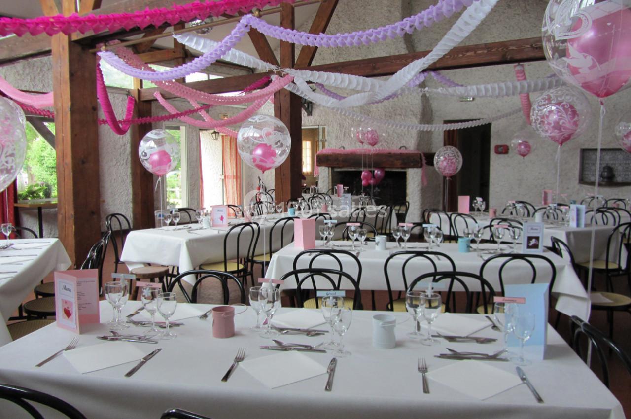 Salle décorée pour une réception avec tables dressées, guirlandes colorées et ballons suspendus.