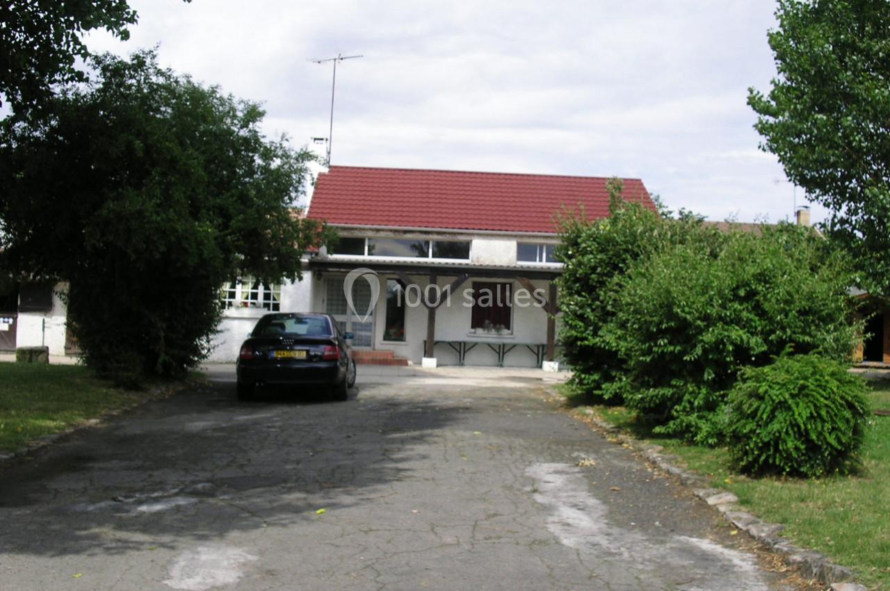 Maison avec toit rouge, allée asphaltée, voiture stationnée devant et arbres entourant la propriété.