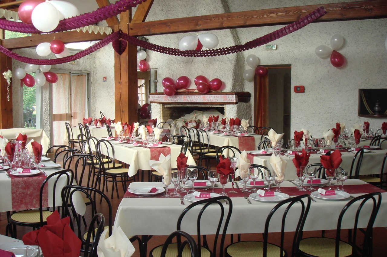 Salle décorée pour un événement avec tables dressées, nappes blanches et rouges, ballons et guirlandes suspendues.
