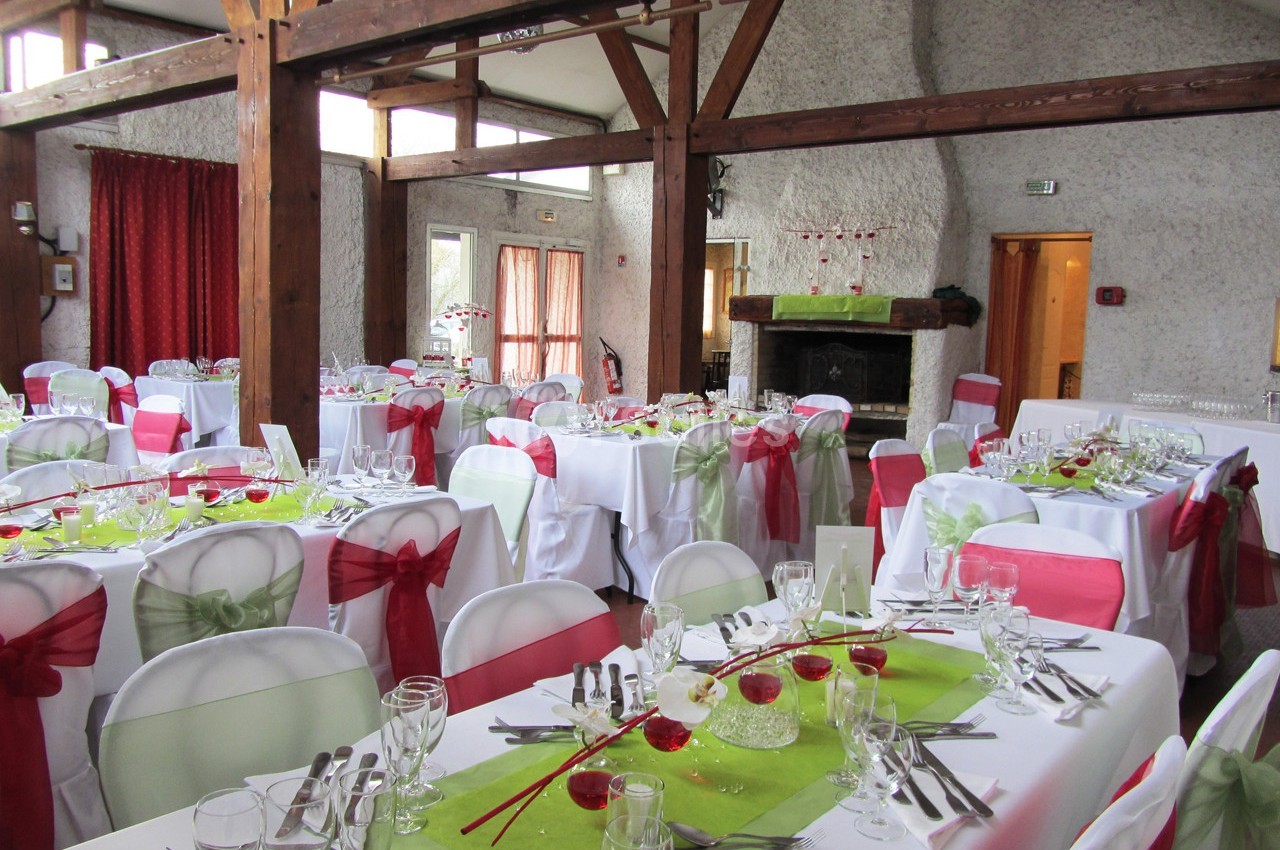 Salle de réception décorée avec des nappes blanches, des rubans colorés sur les chaises et des tables dressées.