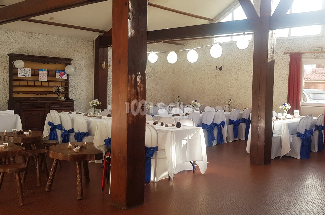 Salle de réception décorée avec des tables blanches, des chaises ornées de nœuds bleus et des guirlandes lumineuses…