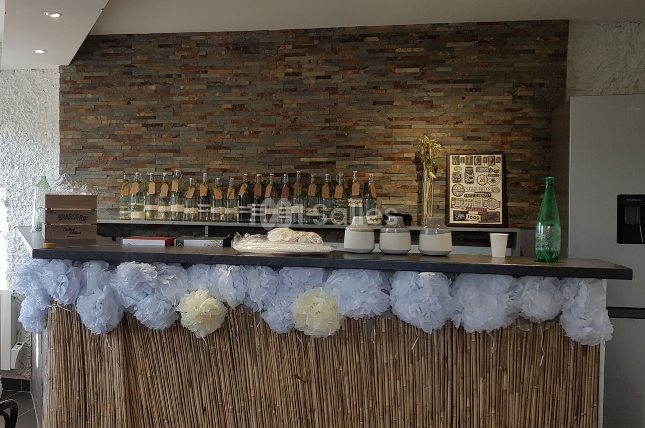Comptoir décoré de fleurs en papier blanc et bleu, avec des bouteilles alignées sur une étagère en arrière-plan.