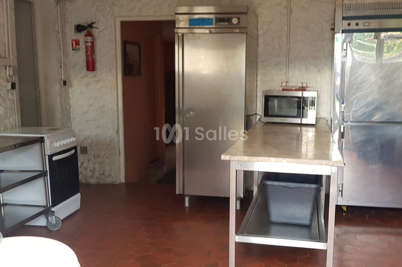 Cuisine professionnelle avec sol en carrelage rouge, équipée d'un four, d'un micro-ondes, d'un réfrigérateur et d'un plan de…