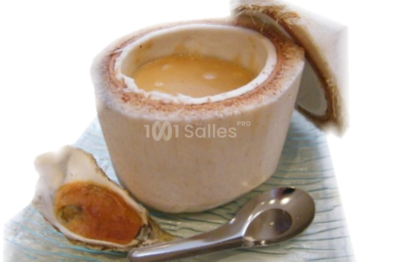 Noix de coco ouverte contenant un liquide, accompagnée d'une huître et d'une cuillère sur une surface texturée.