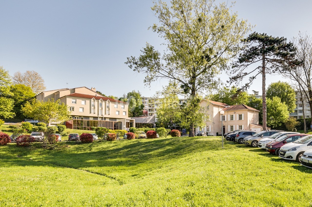 Bâtiments résidentiels entourés d'arbres et de pelouses, avec un parking rempli de voitures au premier plan.