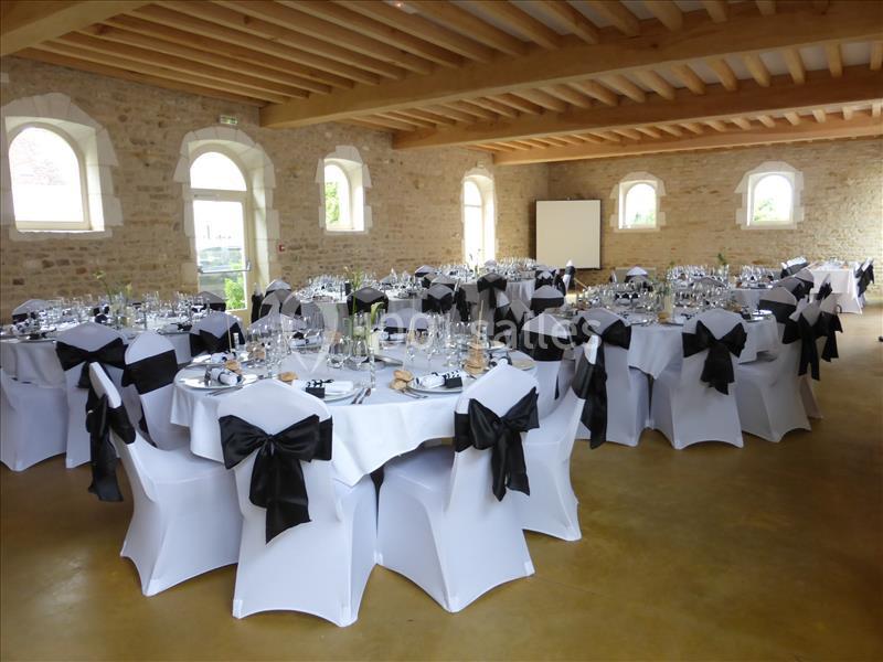 Salle de réception avec tables rondes dressées, nappes blanches et chaises décorées de nœuds noirs.