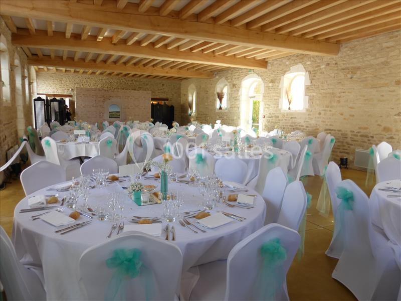 Salle de réception décorée, tables rondes dressées avec nappes blanches et chaises ornées de nœuds verts.