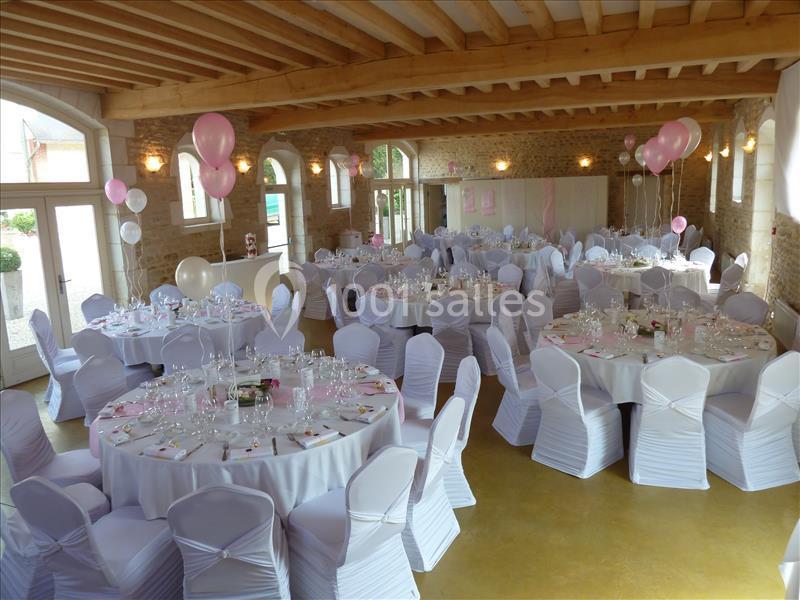 Salle de réception décorée avec des ballons roses et blancs, tables rondes dressées avec nappes blanches et chaises…