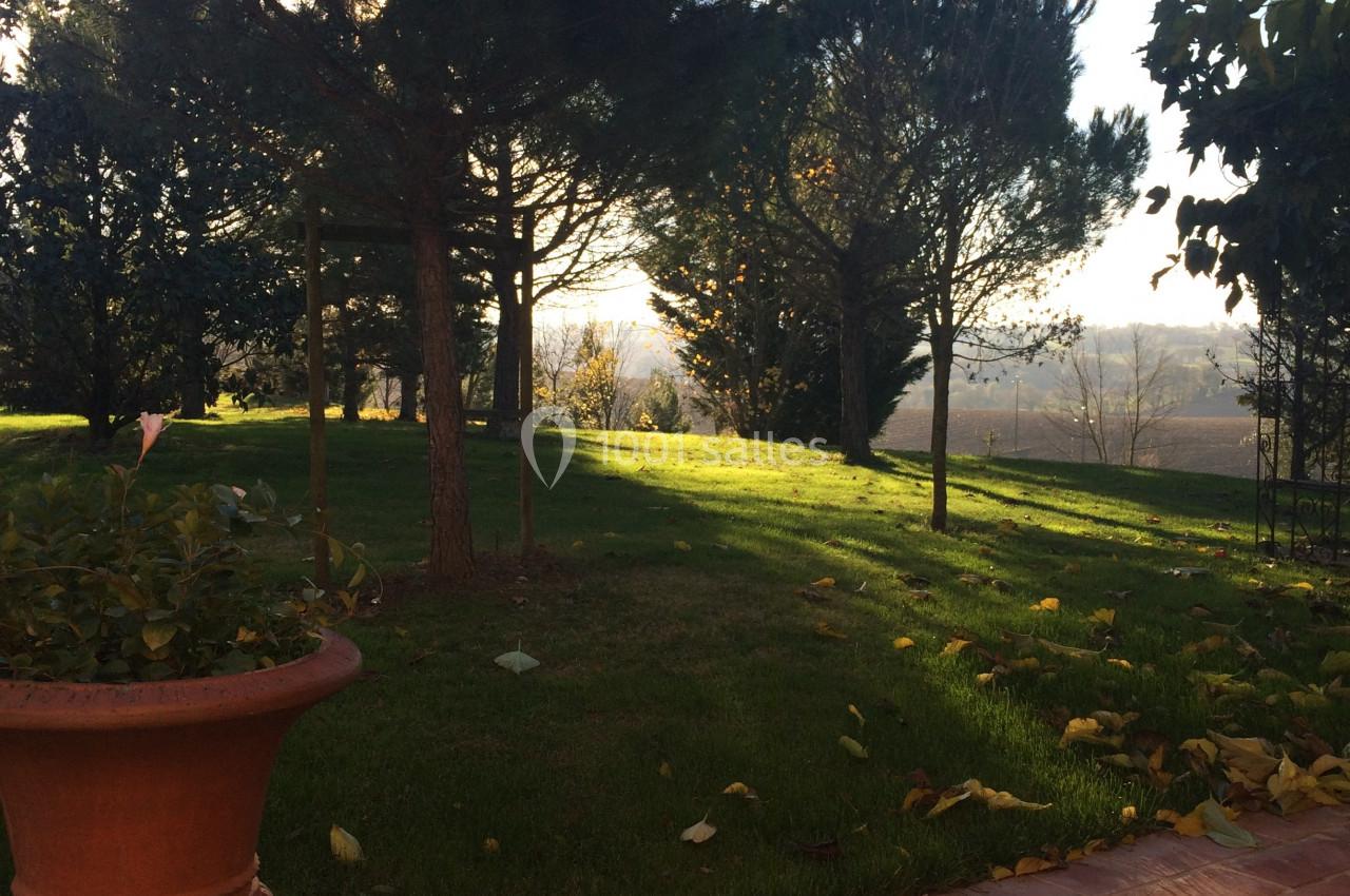 Jardin avec pelouse, arbres et pot en terre cuite au premier plan, éclairé par une lumière douce en fin de journée.