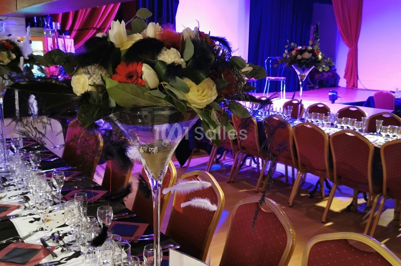 Décoration de table avec des bouquets de fleurs dans des vases hauts, disposée dans une salle de réception éclairée.