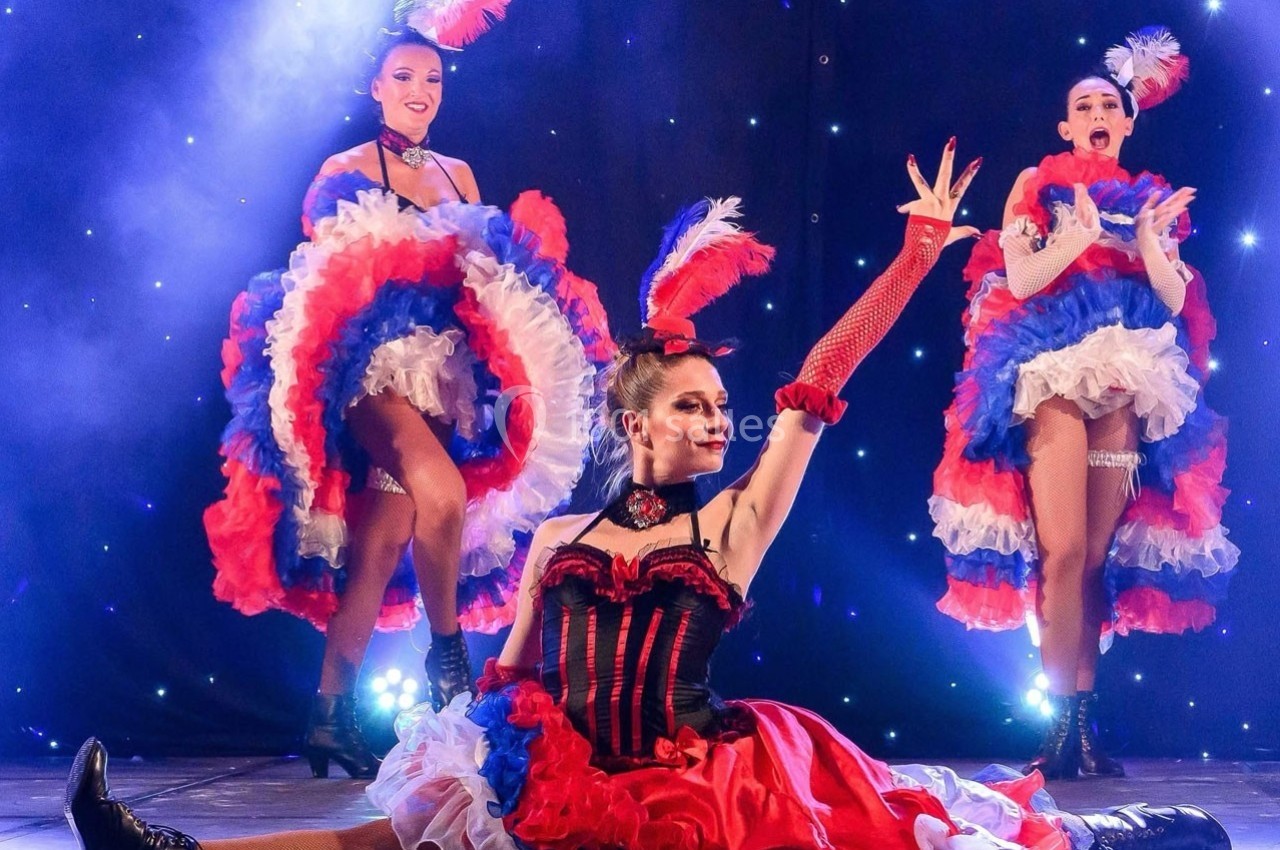 Danseuses en costumes colorés exécutant une performance de French cancan sur une scène illuminée.