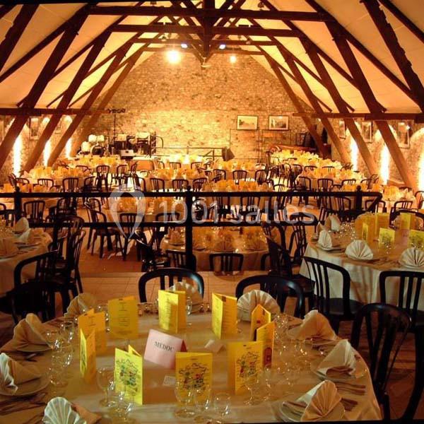 Salle de réception avec tables rondes dressées, nappes blanches, serviettes pliées et menus jaunes, sous une charpente en…