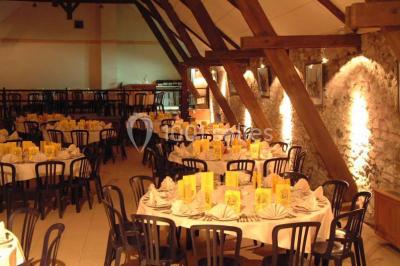 Table dressée avec nappes jaunes, seaux à champagne et verres, sous un grand parasol rouge devant un bâtiment en pierre.
