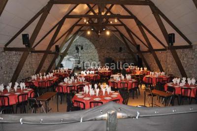 Table dressée avec nappes jaunes, seaux à champagne et verres, sous un grand parasol rouge devant un bâtiment en pierre.