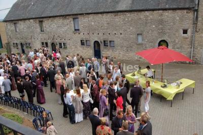 Table dressée avec nappes jaunes, seaux à champagne et verres, sous un grand parasol rouge devant un bâtiment en pierre.