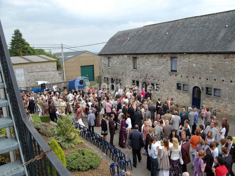 Groupe de personnes rassemblées dans une cour pavée entourée de bâtiments en pierre, lors d'un événement en plein air.