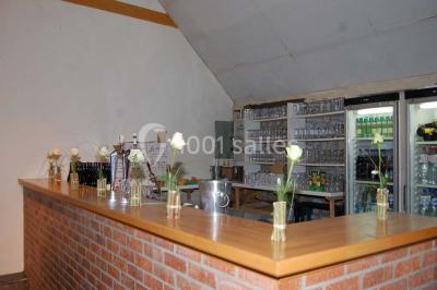 Table dressée avec nappes jaunes, seaux à champagne et verres, sous un grand parasol rouge devant un bâtiment en pierre.