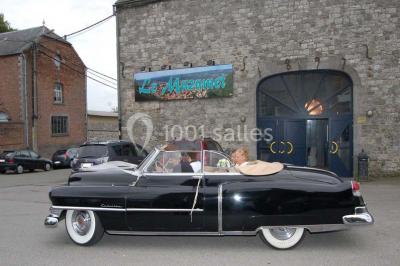 Table dressée avec nappes jaunes, seaux à champagne et verres, sous un grand parasol rouge devant un bâtiment en pierre.