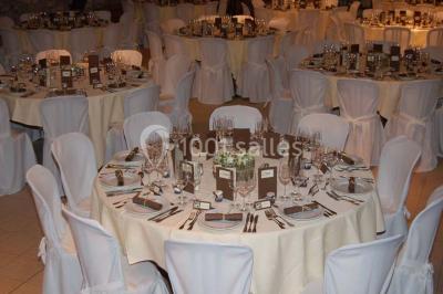 Table dressée avec nappes jaunes, seaux à champagne et verres, sous un grand parasol rouge devant un bâtiment en pierre.