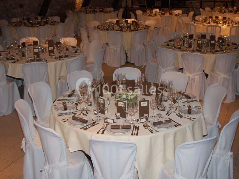 Salle de réception avec tables rondes dressées, nappes blanches, chaises couvertes et décorations de table élégantes.