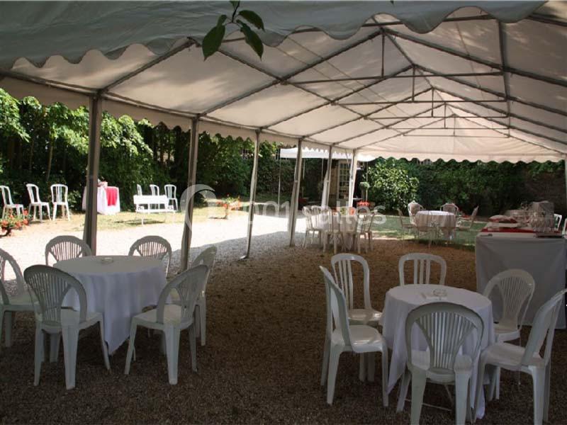 Tente blanche installée dans un jardin, avec des tables et des chaises en plastique disposées sur un sol en gravier.
