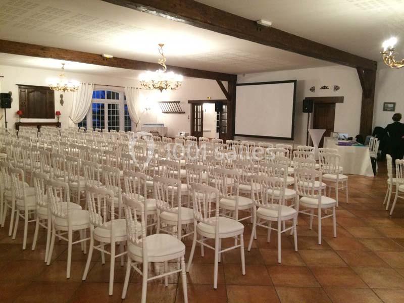 Salle de réception avec rangées de chaises blanches alignées face à un écran de projection.
