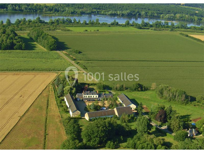 Vue aérienne d'une ferme entourée de champs et de verdure, avec une rivière visible à l'arrière-plan.