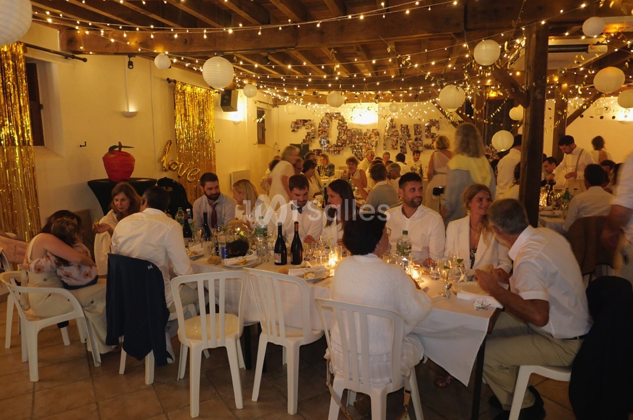 Salle décorée avec des guirlandes lumineuses et des invités assis à des tables lors d'une fête ou d'un événement.
